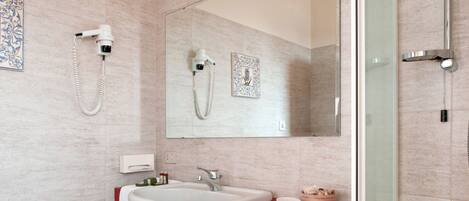 Un baño moderno con un espejo grande, un lavamanos blanco, una encimera roja y una zona de ducha.