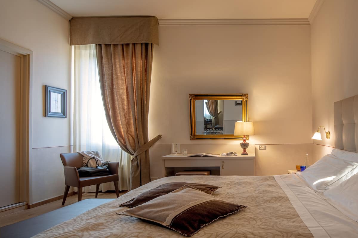 A hotel room with a bed, a desk, a chair, a lamp, and a mirror.