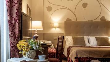 Una habitación de hotel con cama, mesita de noche, lámpara, flores y una pared con diseño floral.