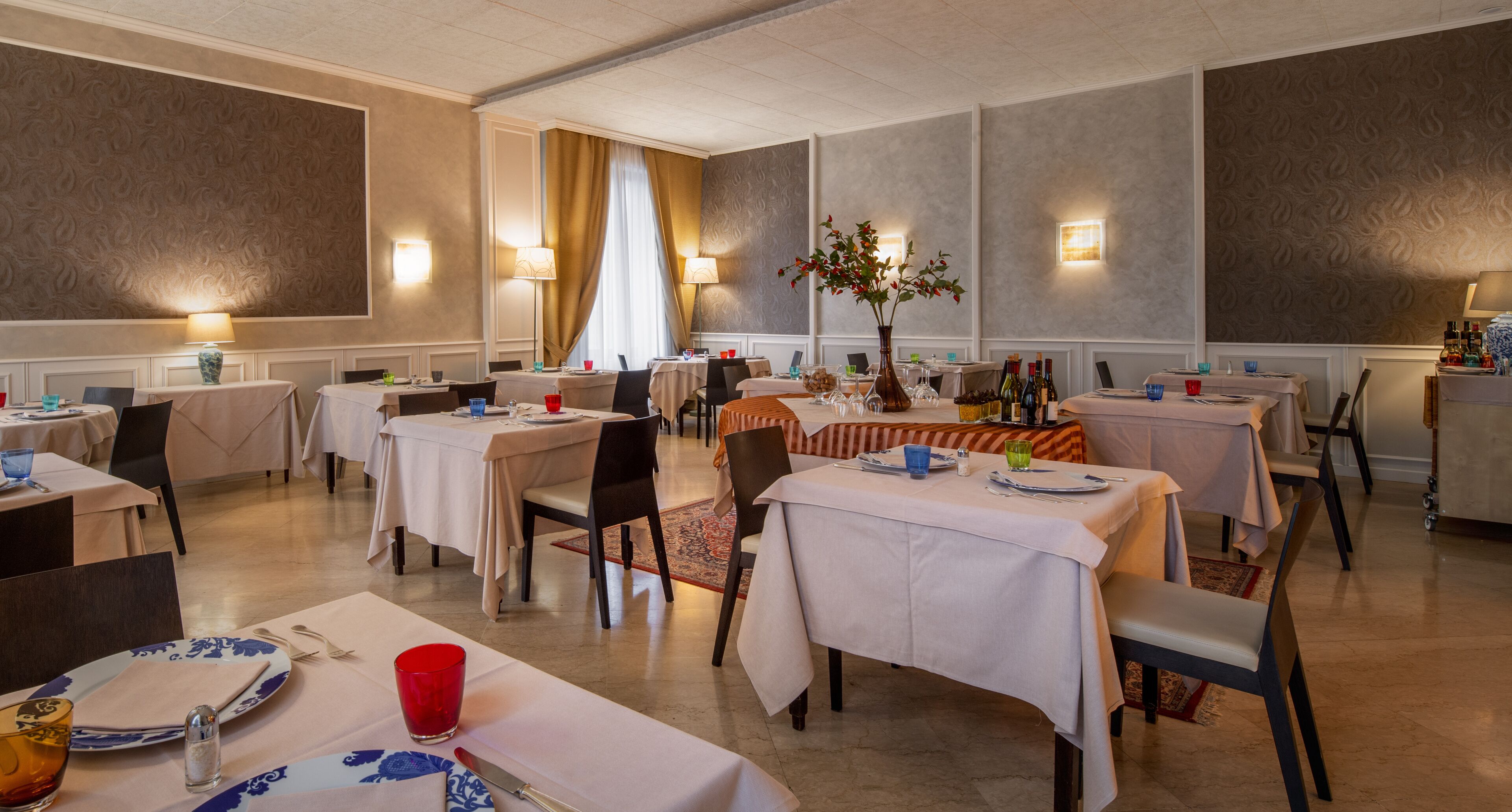 Un comedor con varias mesas, sillas y un centro de mesa decorativo con planta.