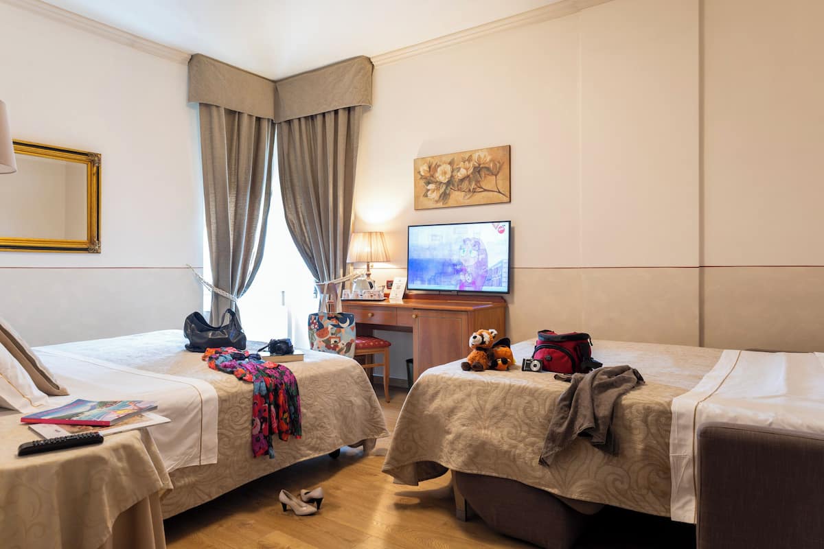 A hotel room with two beds, a desk with a computer, a TV, and a window with curtains.