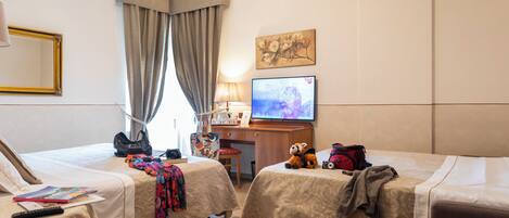A hotel room with two beds, a desk with a computer, a TV, and a window with curtains.
