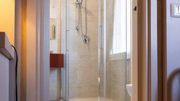 A modern bathroom with a glass shower enclosure, a white sink, and a beige tiled floor.