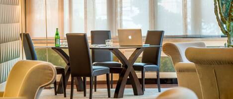 Une chambre d’hôtel moderne dotée d’un coin repas comprenant une table en verre, quatre chaises et deux ordinateurs portables.