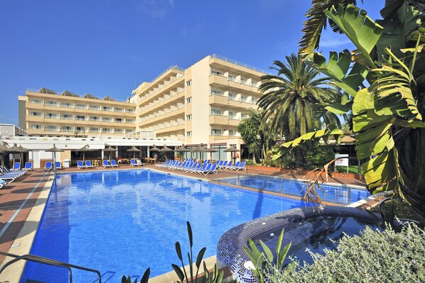 Un hotel con piscina, varios balcones y plantas tropicales.