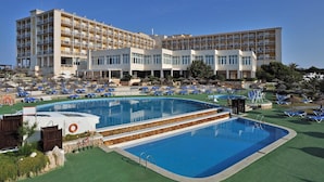 Un hotel con una piscina amplia, varios balcones y un césped bien cuidado.