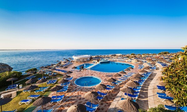 Un resort con una piscina grande, tumbonas y vistas al mar.