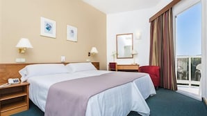 Una habitación de hotel con cama, mesitas de noche, escritorio, silla, ventana con cortinas y vistas.