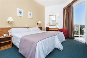 A hotel room with a bed, bedside tables, a desk, a chair, a window with curtains, and a view. - Globales Playa Santa Ponsa (Calvia)