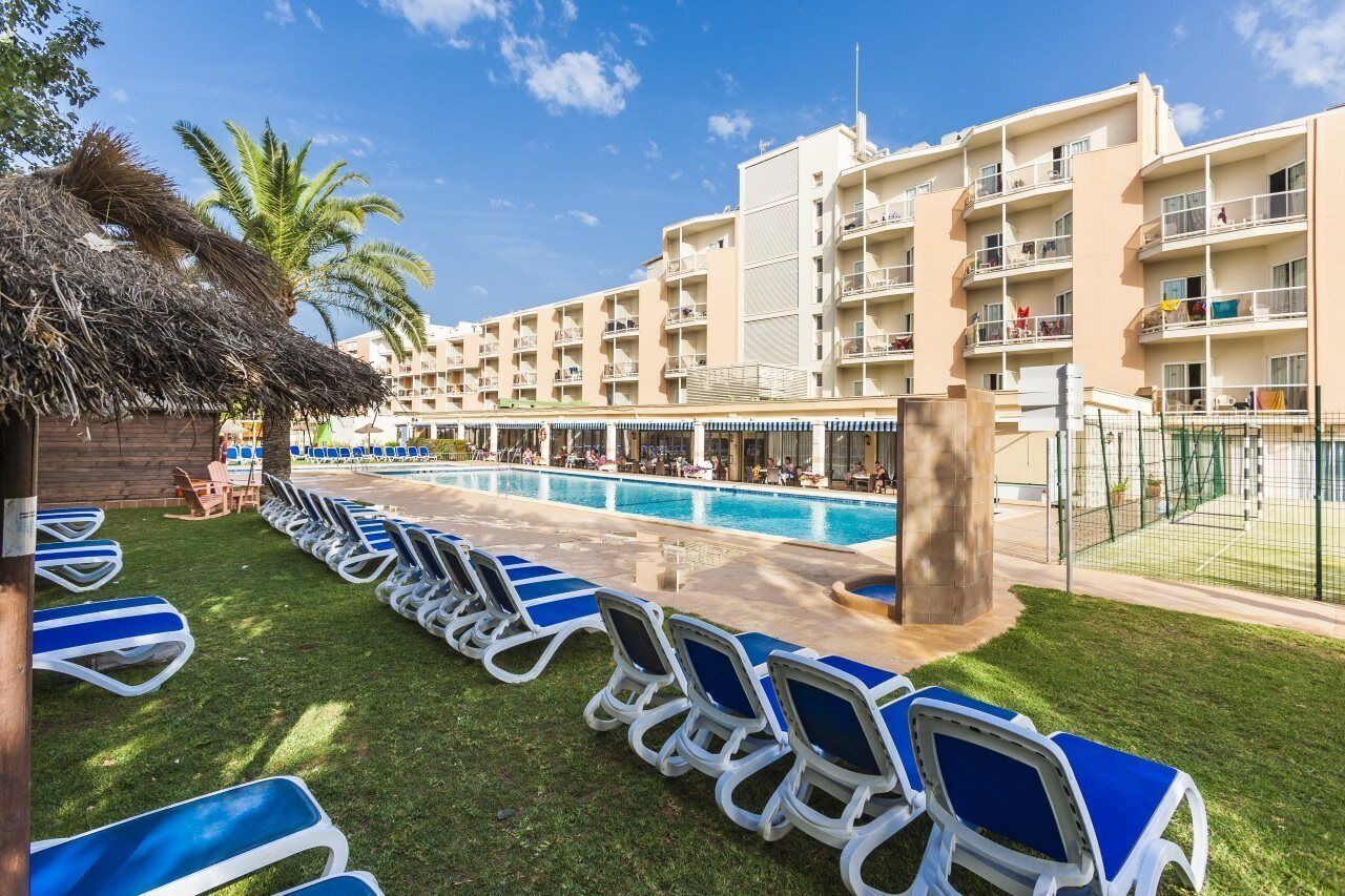 Un hotel con piscina, sillas de descanso y una palmera.