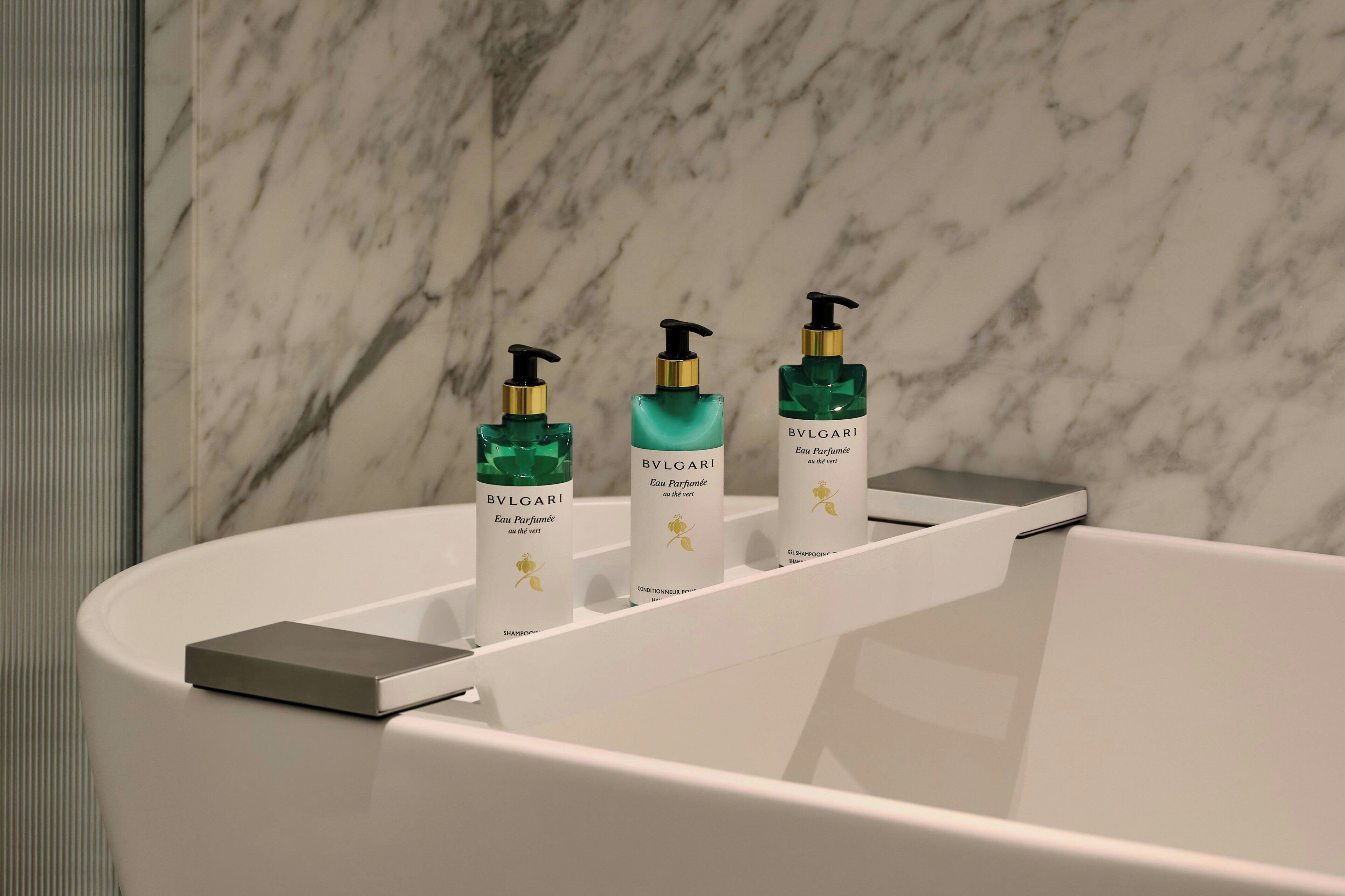 A bathroom with a marble wall, three BVLGARI perfume bottles, and a modern faucet.