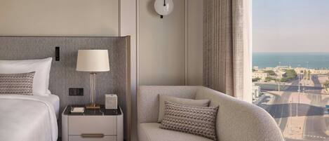 A hotel room with a bed, nightstand, lamp, and a sofa with a view of the city.