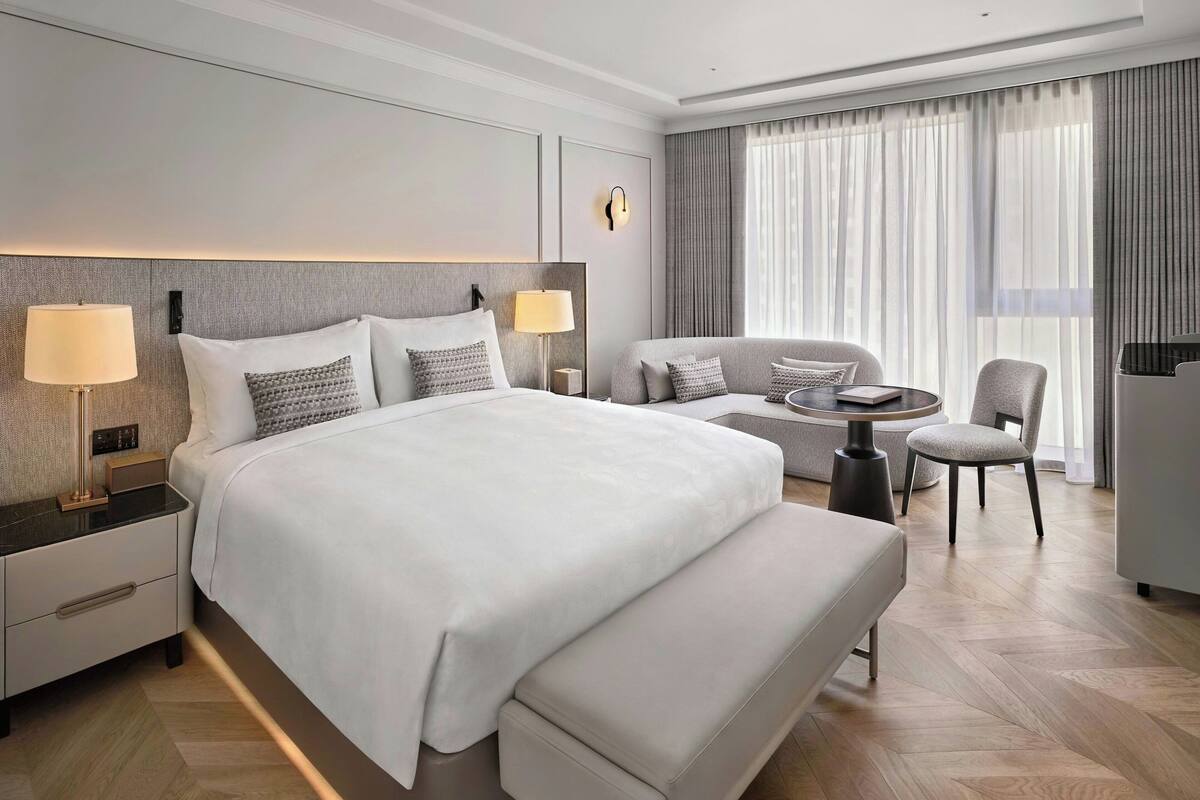 Une chambre d’hôtel moderne avec un grand lit, des lampes de chevet, un canapé, une petite table et un téléviseur.