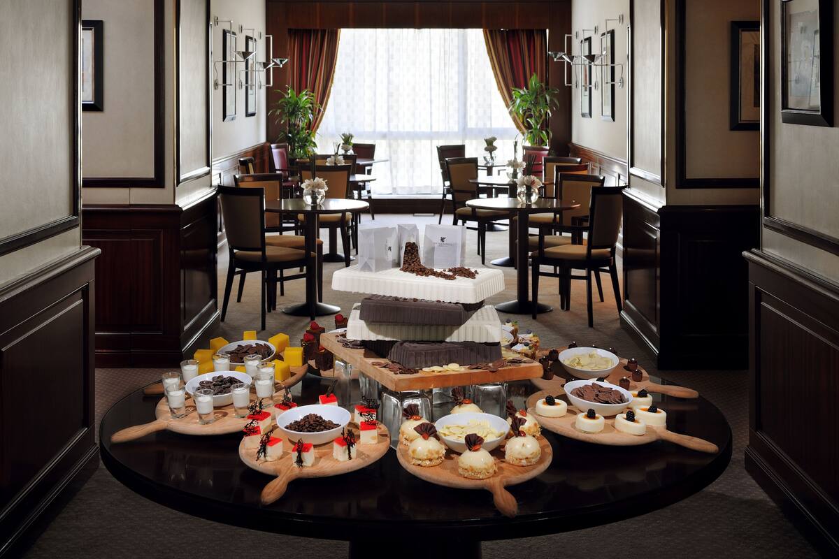 Un espace repas avec une grande table ronde, dressée avec divers desserts et boissons, entourée de chaises et de petites tables.