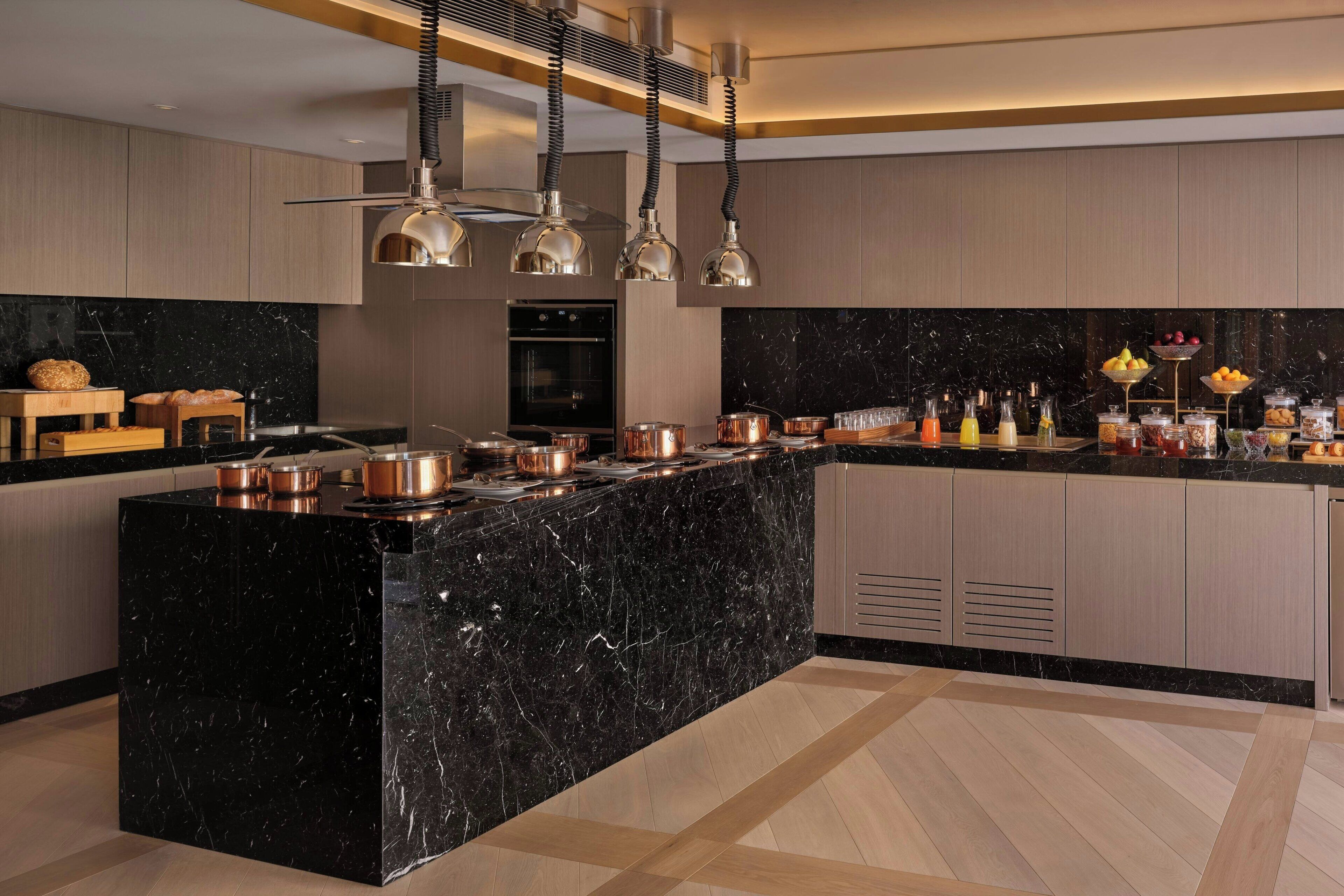 A modern kitchen with a black marble island, copper cookware, and a variety of breakfast items.