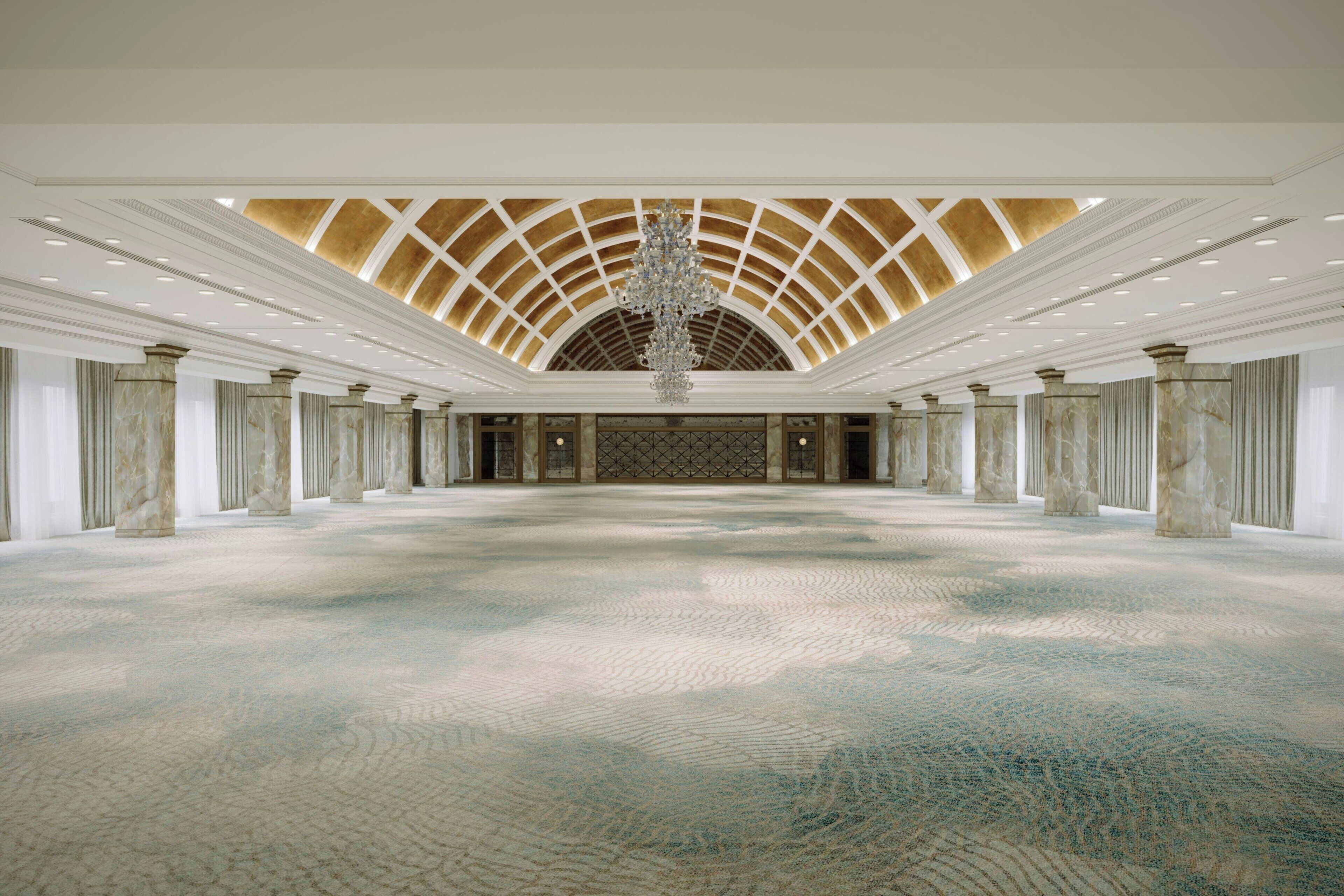 A spacious hall with a high arched ceiling, marble columns, and a central chandelier.