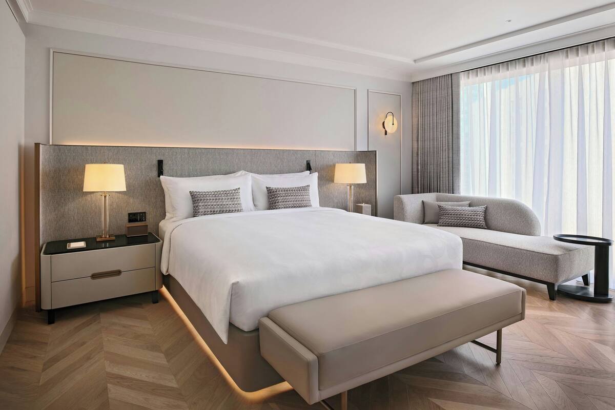 Une chambre d’hôtel moderne dotée d’un grand lit, de lampes de chevet, d’un banc, d’un canapé et offrant une vue sur l’extérieur.