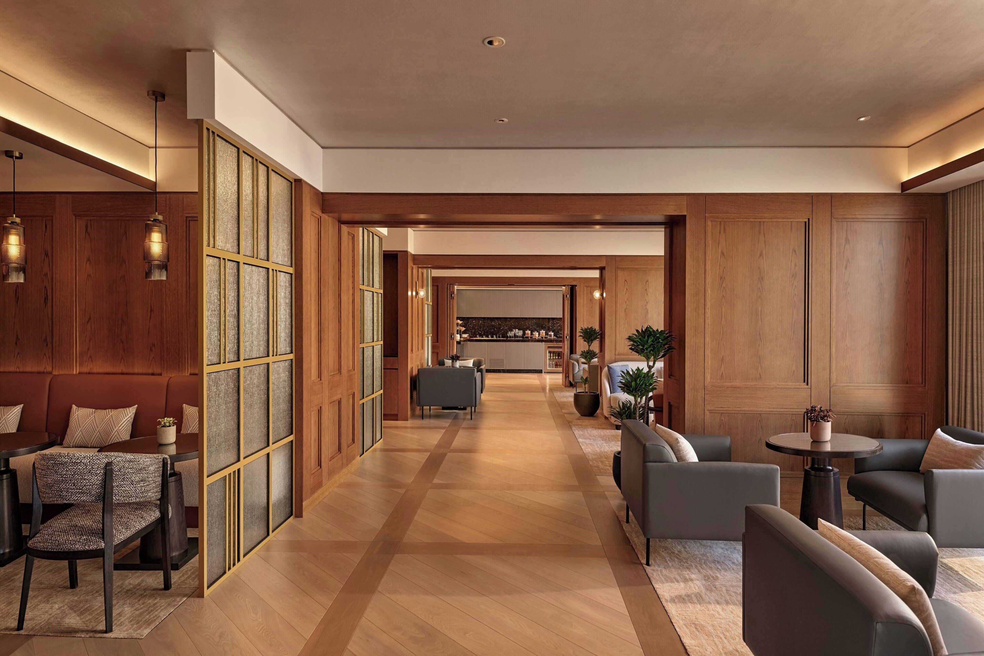 Un amplio vestíbulo de hotel con piso de madera, zonas de estar y vista hacia la cocina.