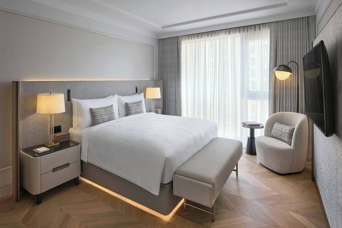 Une chambre d’hôtel moderne avec un grand lit, des lampes de chevet, un banc, une chaise et un téléviseur.