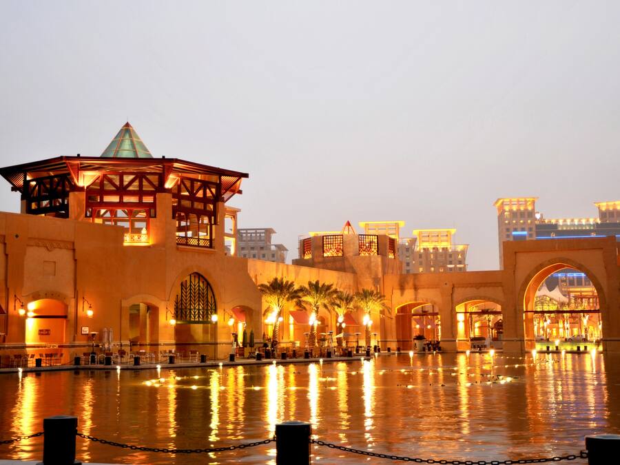 A waterfront hotel with a prominent glass-roofed pavilion, arched walkways, and a reflection pool.