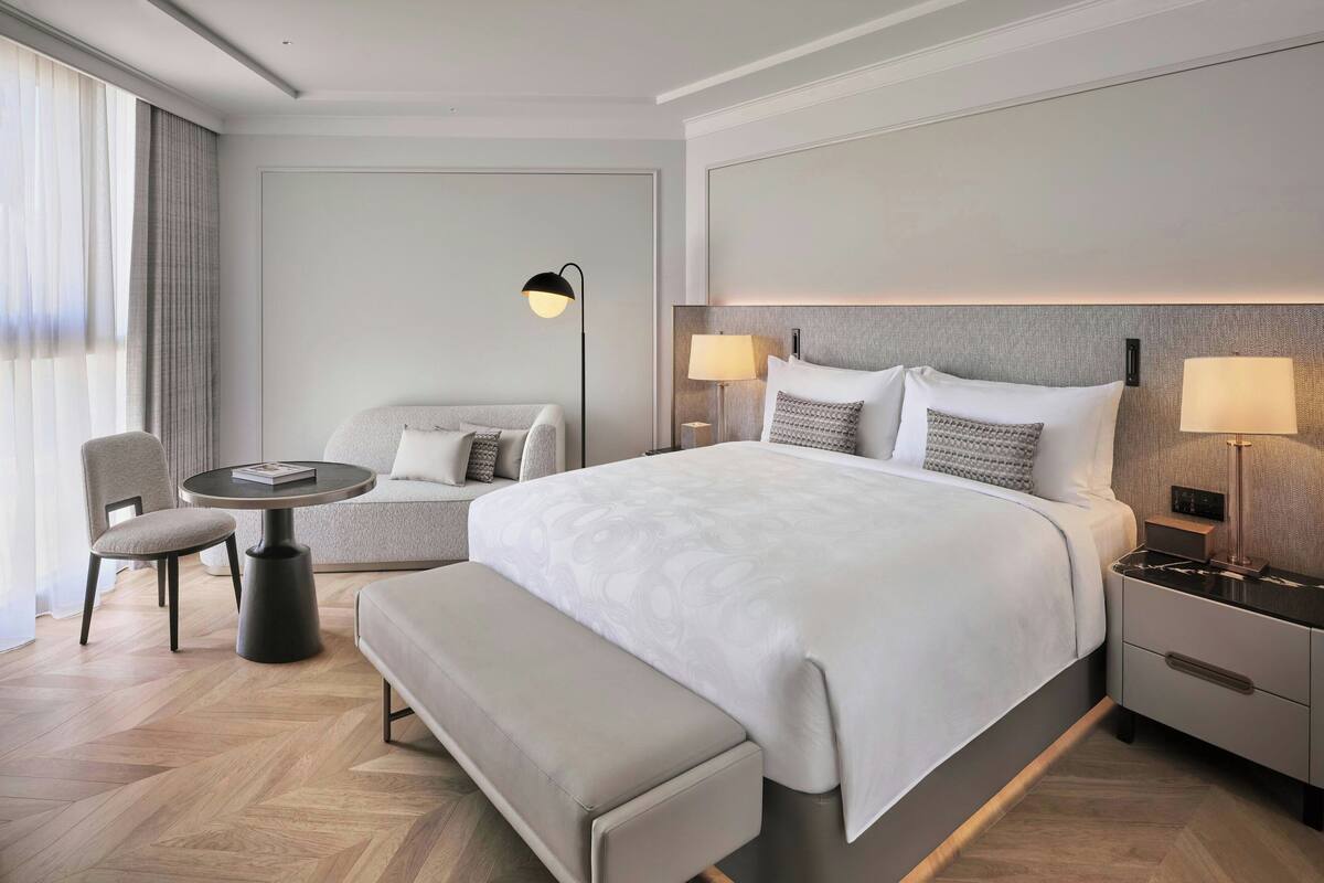 Une chambre d’hôtel moderne avec un grand lit, une table de chevet, une chaise, une petite table ronde et un banc.