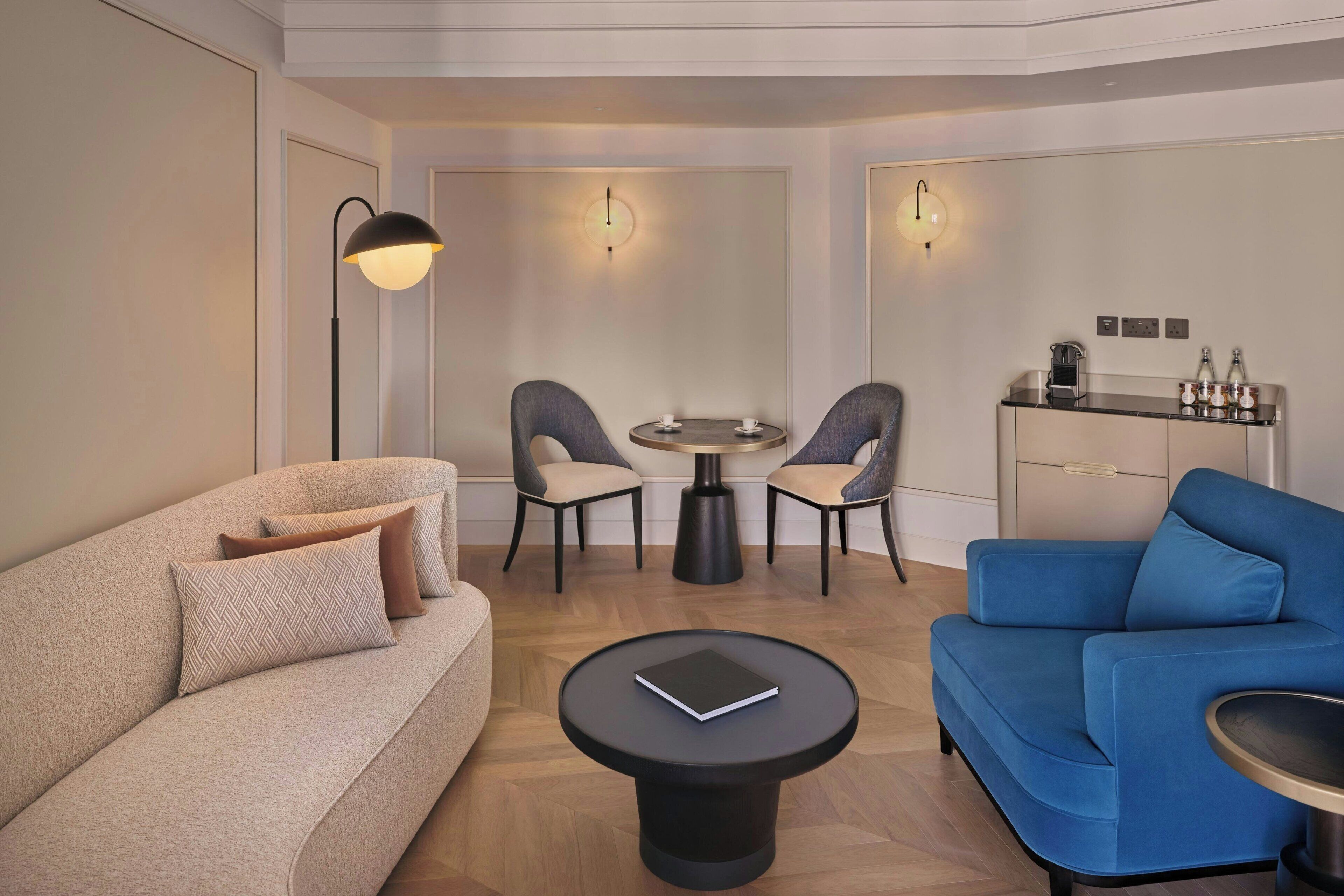 A modern living room with a sofa, a blue armchair, a round coffee table, a small round table with chairs, and a kitchen area with a counter and cabinets.