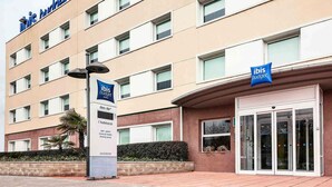 Edifici d'hotel amb diverses plantes, un cartell que indica 'ibis budget hotels' i un cartell de 'des de' amb serveis enumerats.