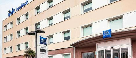 A hotel building with multiple floors, a sign indicating 'ibis budget hotels,' and a sign for 'des de' with amenities listed.