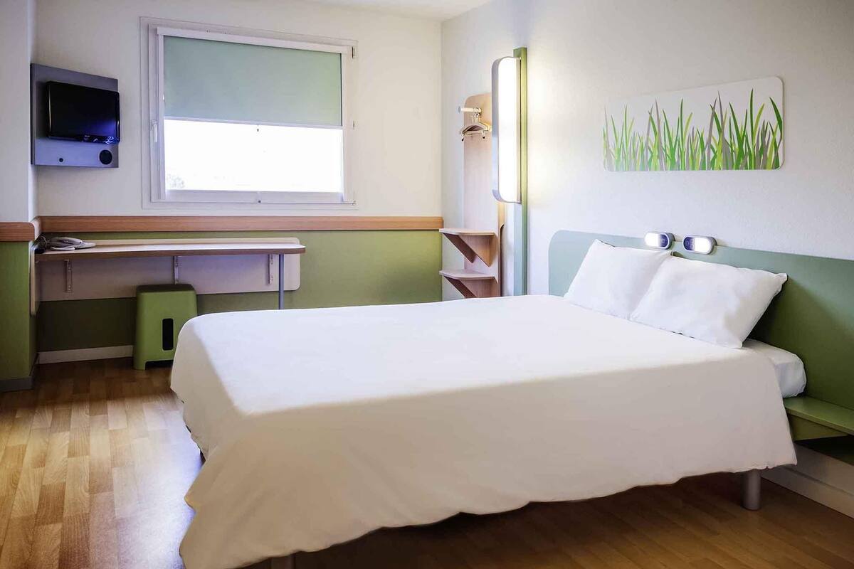 Una habitación de hotel con una cama, un escritorio, una silla, un televisor y un cuadro.