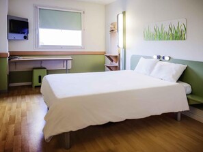 A hotel room with a bed, a desk, a chair, a TV, and a painting.