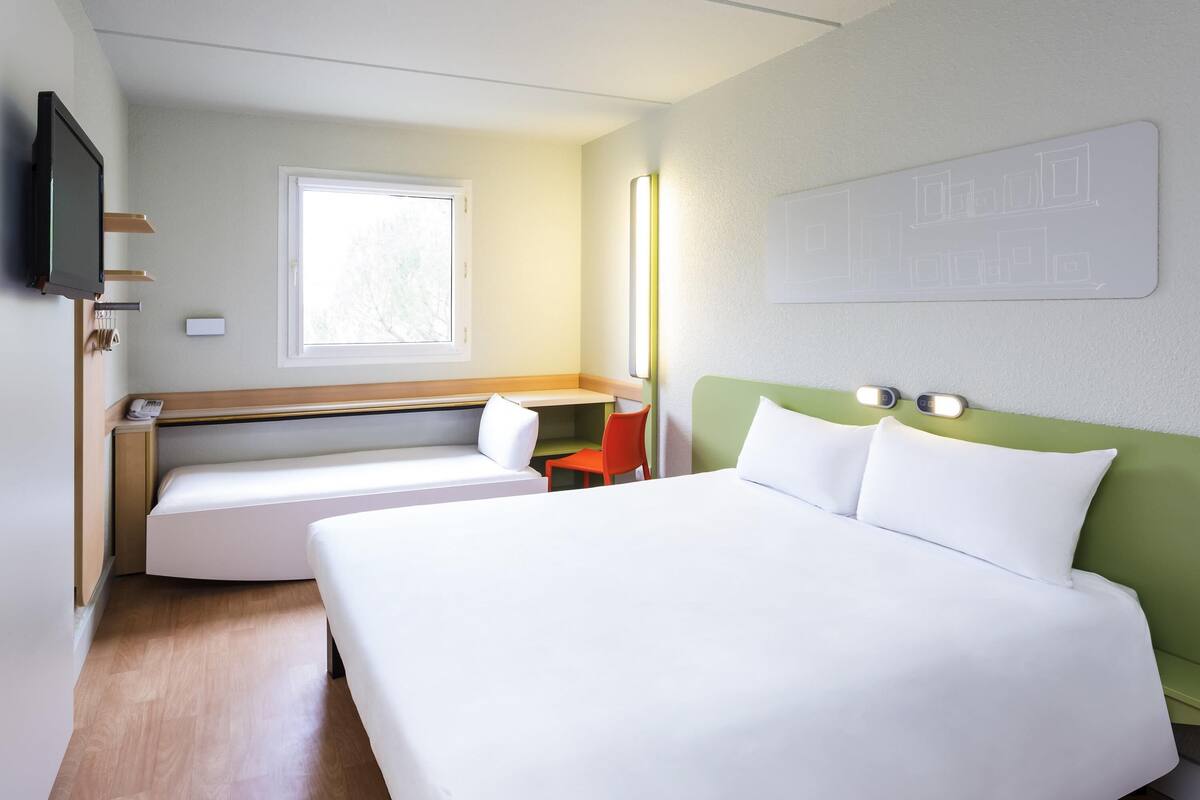 Una habitación de hotel con una cama grande, un escritorio, una silla, un televisor y una ventana.