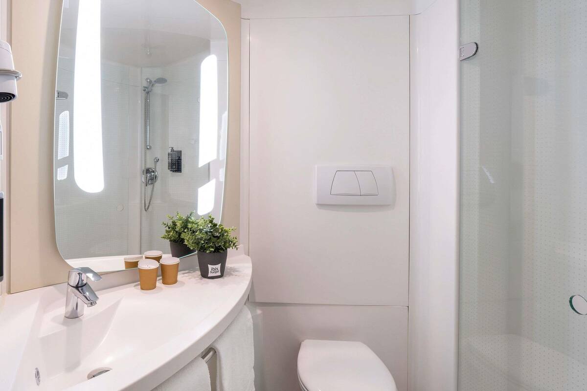 Un baño moderno con un espejo grande, un lavamanos, un inodoro y una ducha.