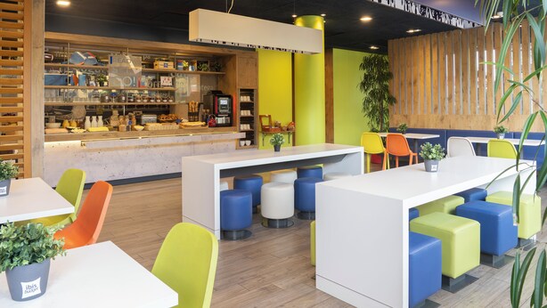 Una cafeteria moderna amb seients de colors, una barra amb diferents productes alimentaris i una paret decorativa de fusta.