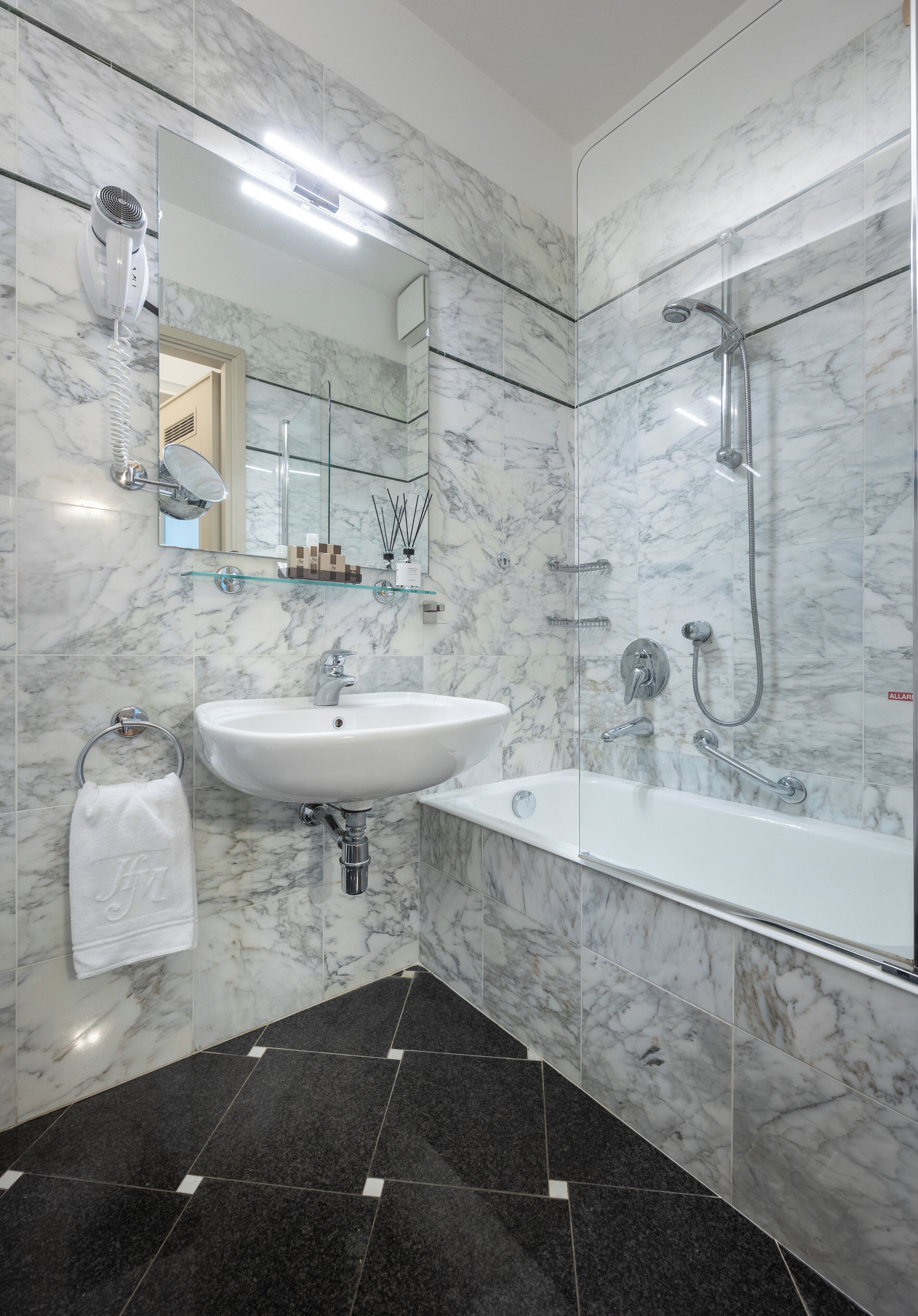 A modern bathroom with a marble sink, a glass-enclosed shower, and a black-tiled floor.