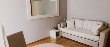 A modern living room with a sofa, a small side table, a round table, and a large mirror on the wall.
