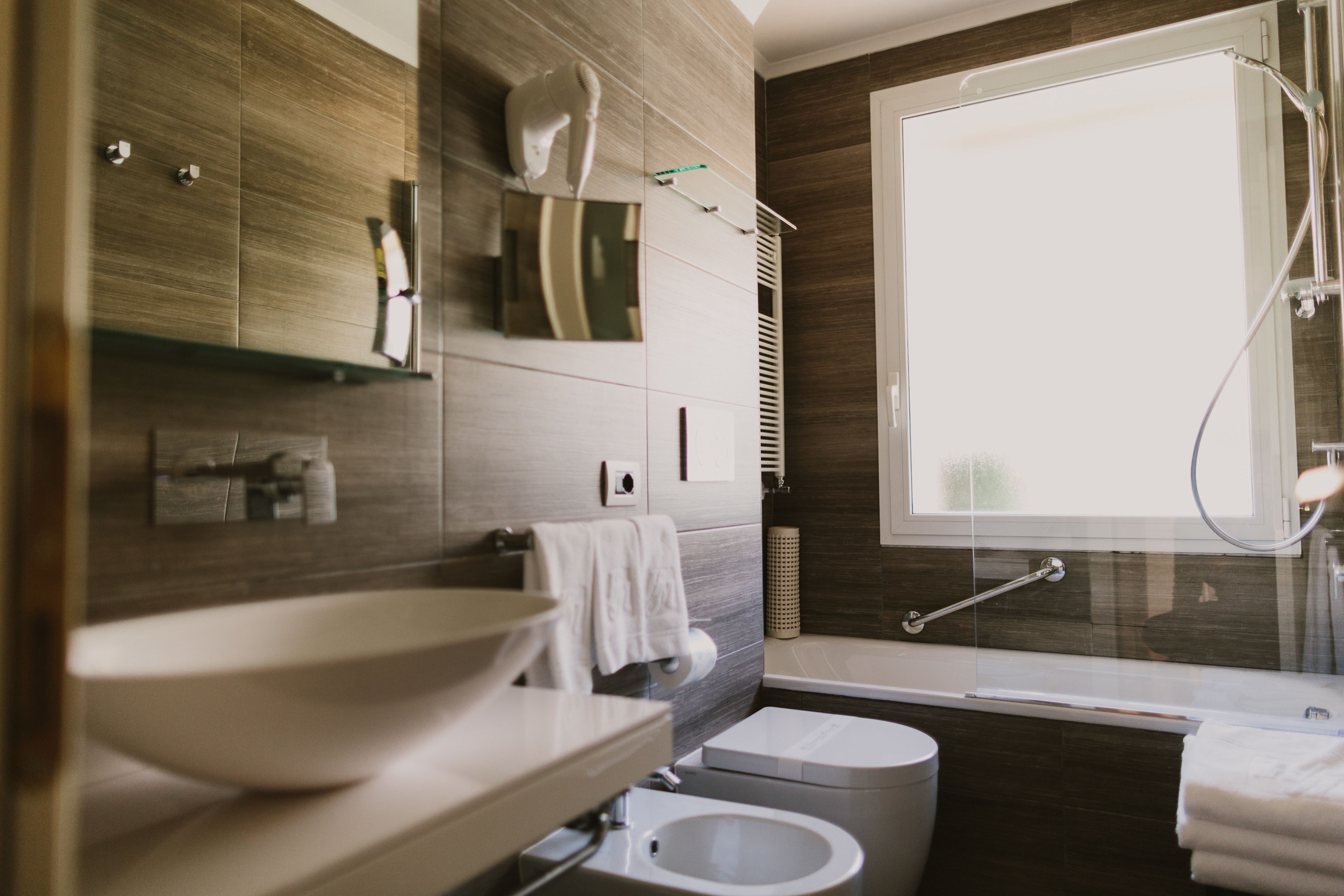 A modern bathroom with a large sink, toilet, and bathtub. There is a window providing natural light and a towel rack.