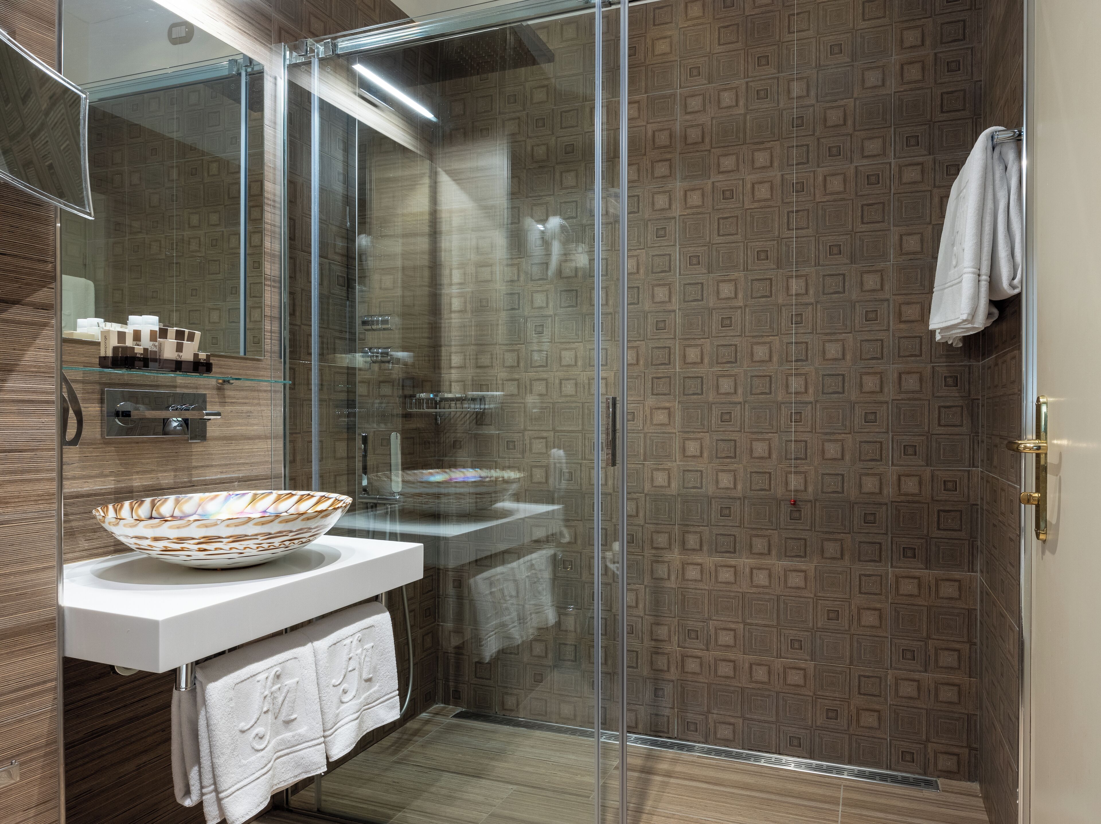 A modern bathroom with a glass-enclosed shower, a white sink with a decorative bowl, and patterned wall tiles.