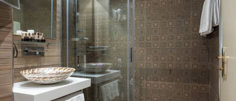 A modern bathroom with a glass-enclosed shower, a white sink with a decorative bowl, and patterned wall tiles.