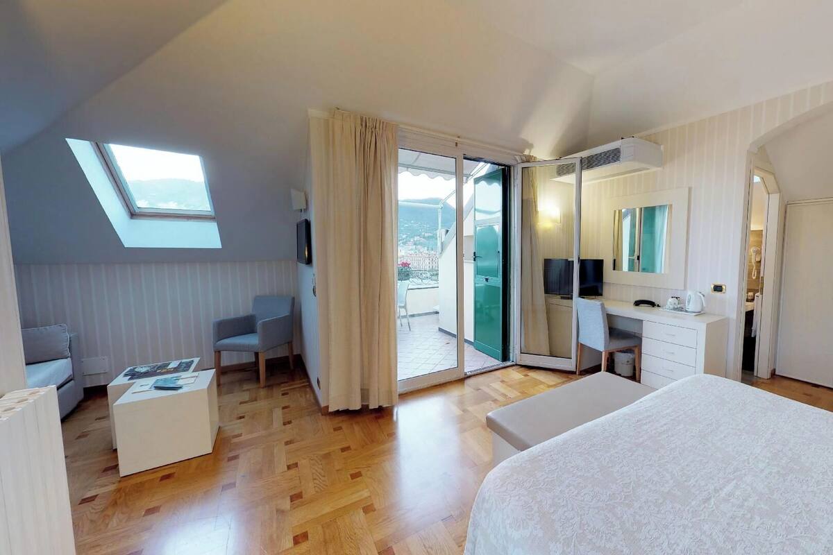 Une chambre d’hôtel moderne dotée d’un grand lit, d’un bureau avec une chaise, d’un balcon avec des rideaux et d’un grand miroir.