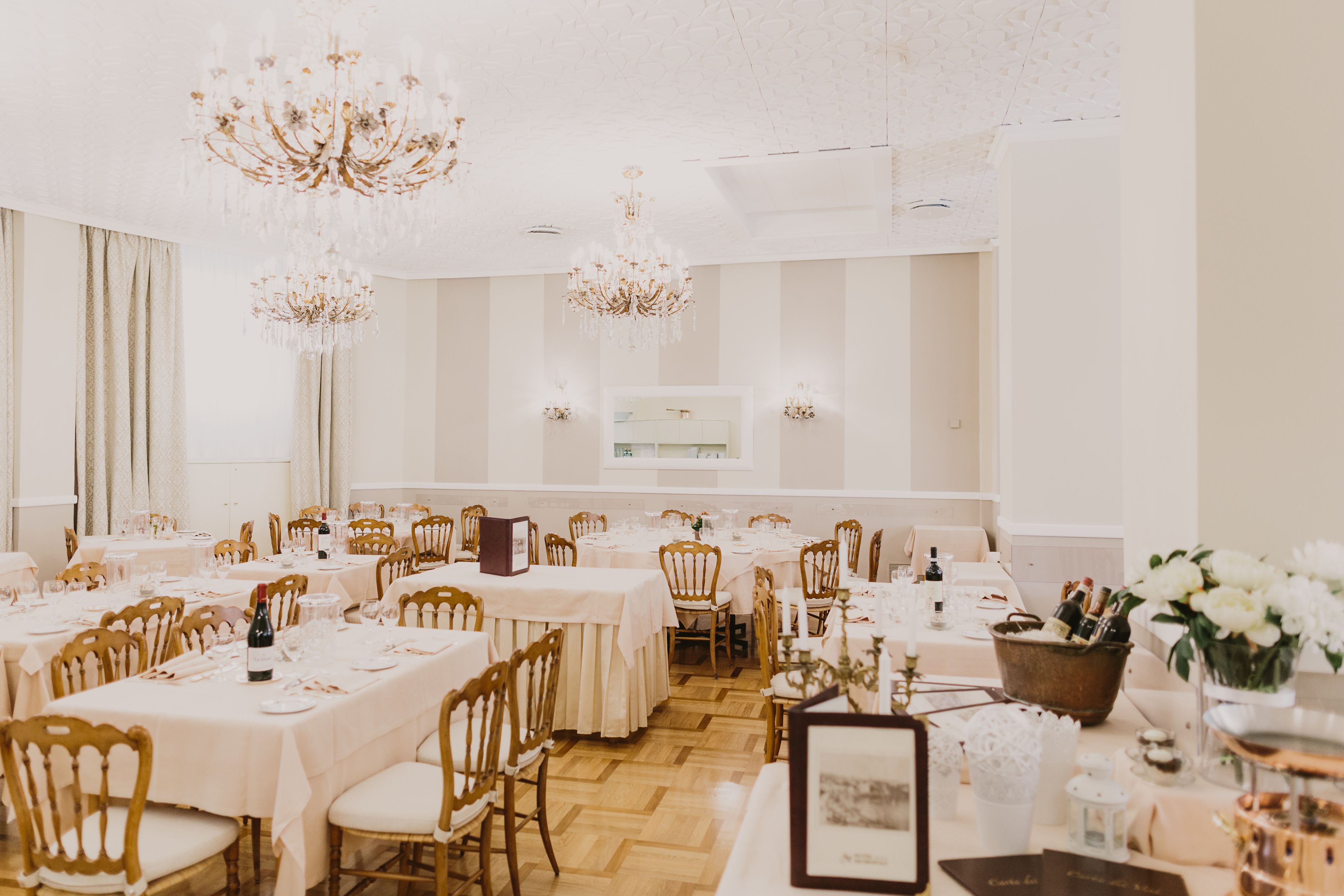 A banquet hall with multiple tables set for dining, chandeliers, and a white interior.