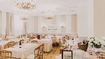 A banquet hall with multiple tables set for dining, chandeliers, and a white interior.