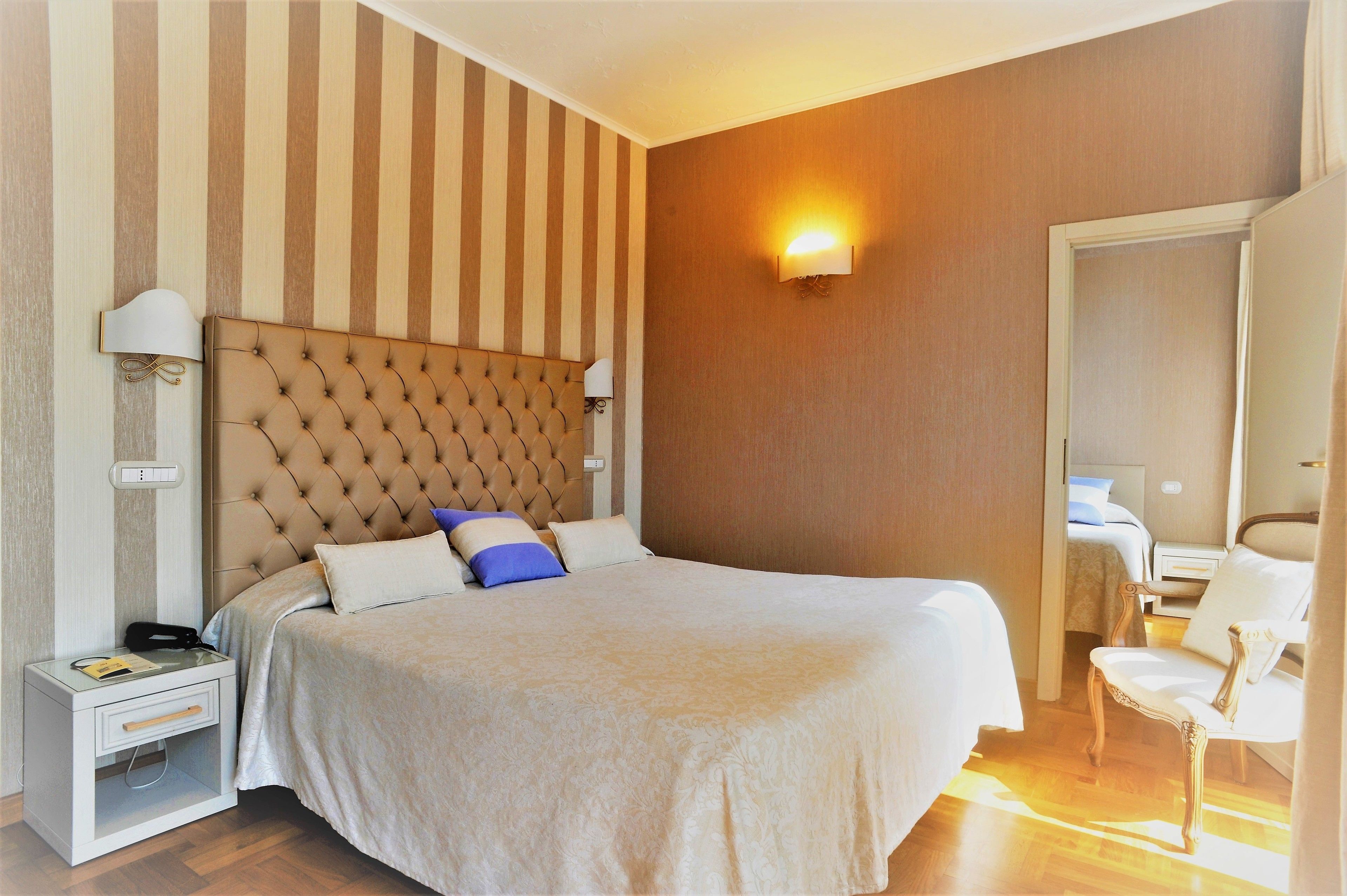 A hotel room with a large bed, a nightstand, a chair, and a wall-mounted lamp.