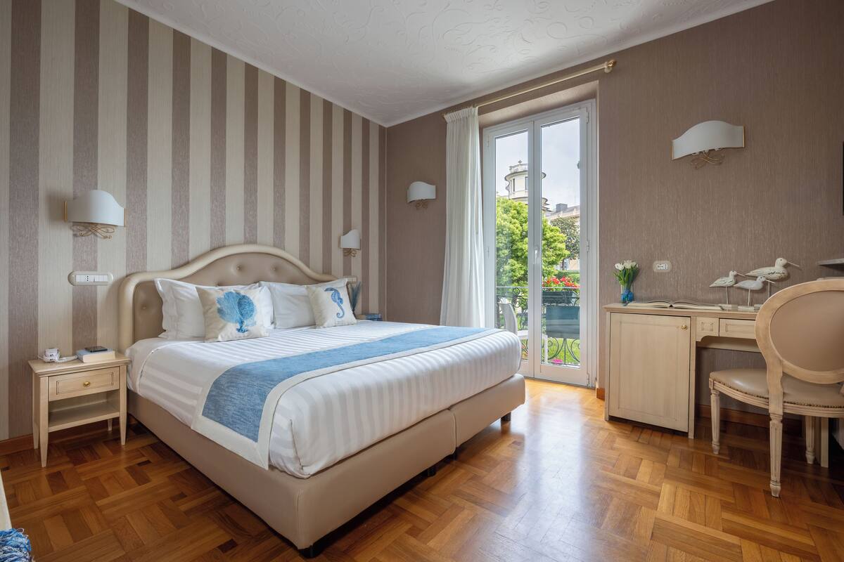 Une chambre avec un grand lit, un bureau et une chaise. Il y a une fenêtre donnant sur un paysage verdoyant.