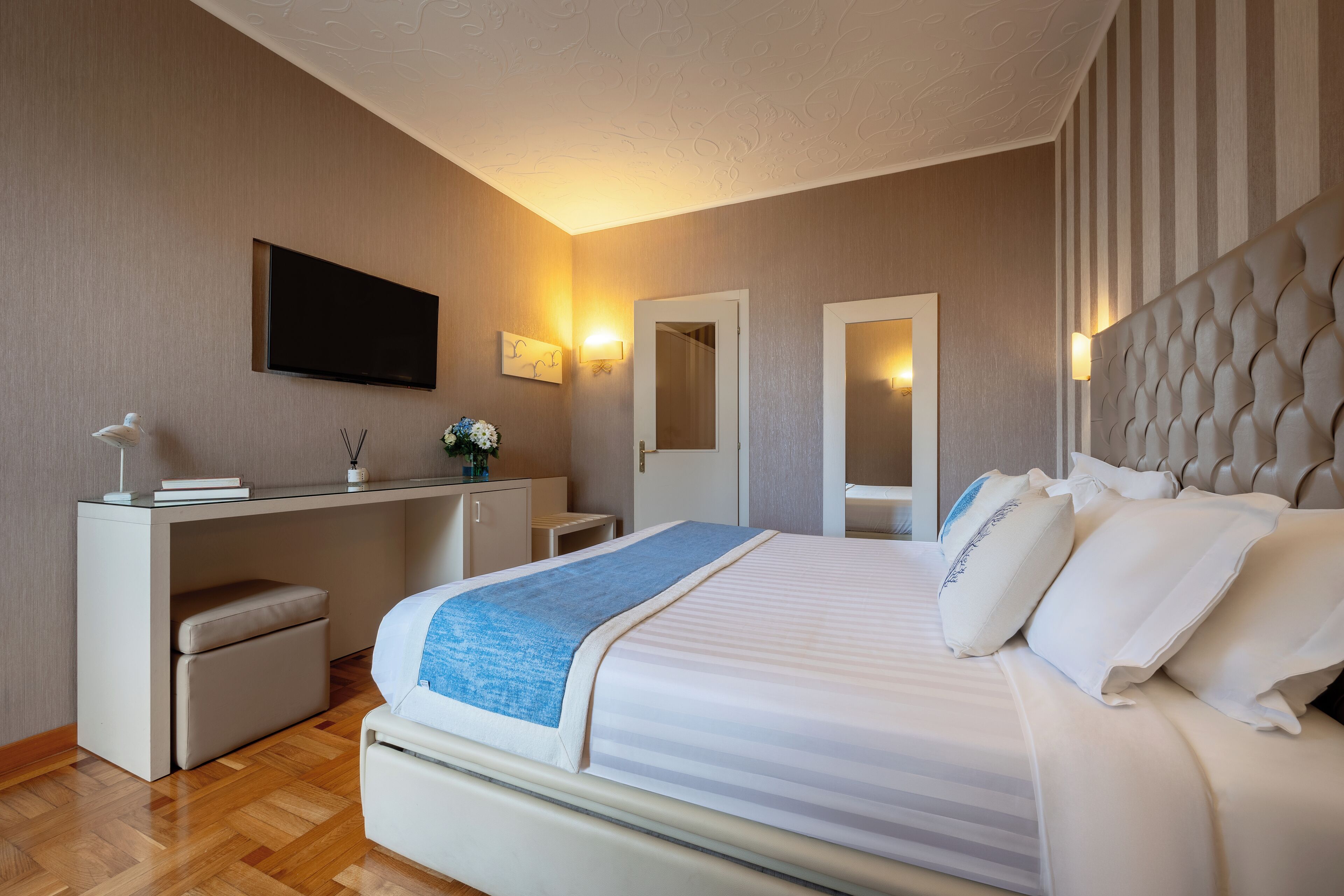 Quarto de hotel moderno com uma cama grande, uma mesa com cadeira, televisão de tela plana e um espelho.