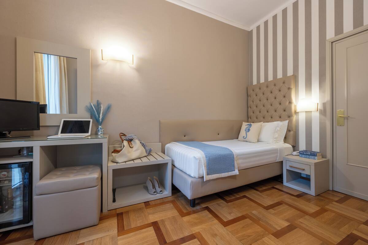 Une chambre d’hôtel comprenant un lit, une table de chevet, une lampe, une télévision et un petit coin salon avec une chaise et une table.