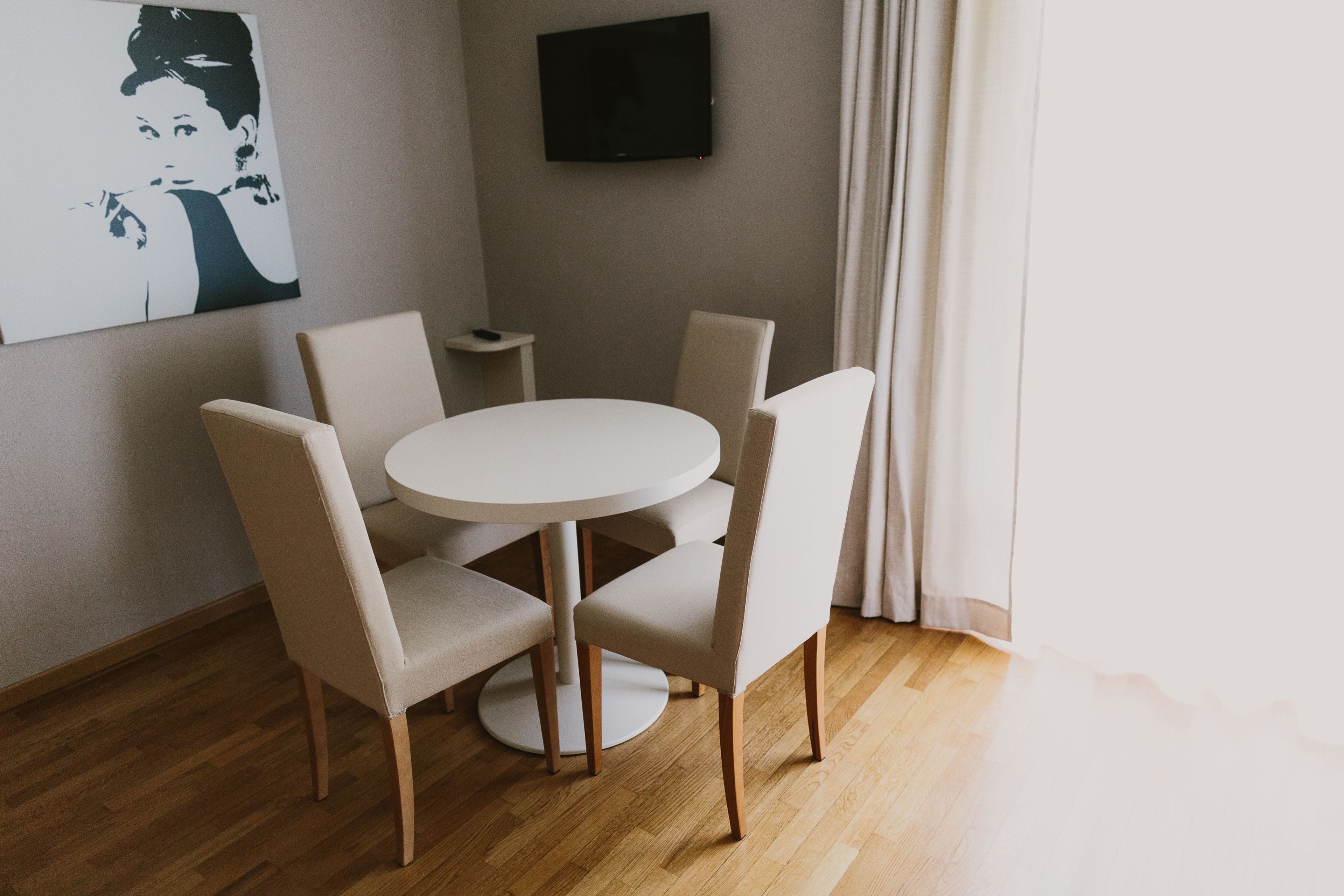 Un'area pranzo con un tavolo rotondo e quattro sedie, una televisione a schermo piatto appesa al muro e un quadro.