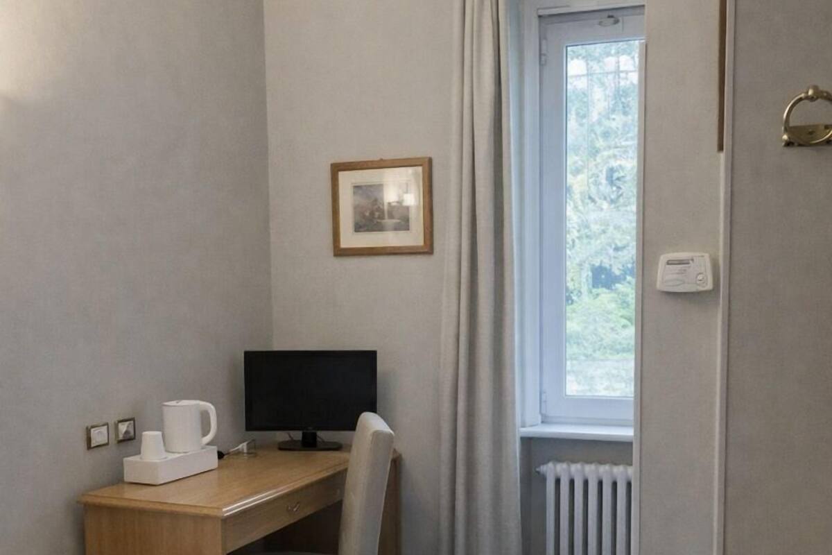 Une chambre d’hôtel équipée d’un lit, d’un bureau, d’une chaise, d’un ordinateur et d’une fenêtre avec des rideaux.