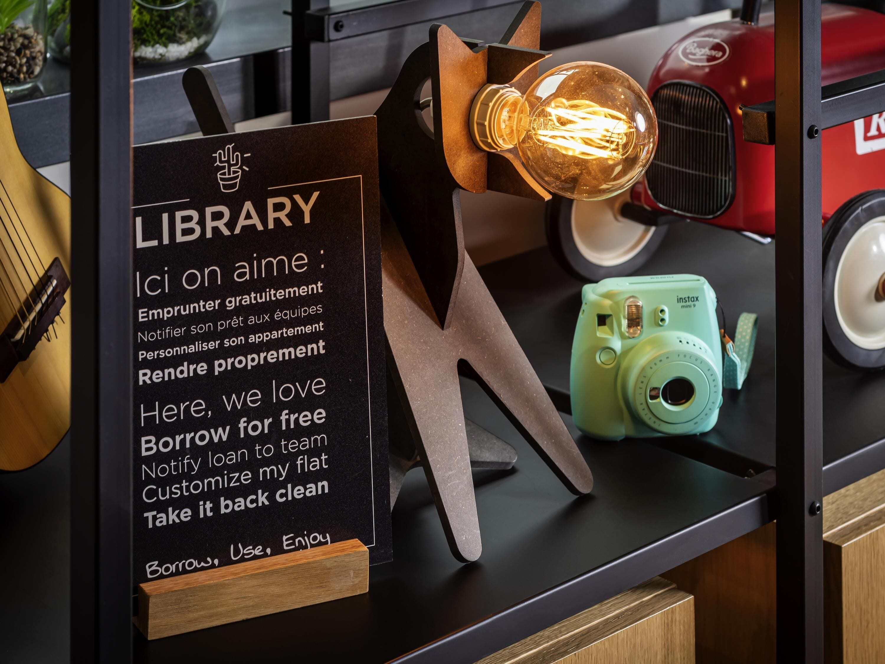 A library sign with a list of services, a vintage light bulb, and a green camera on a counter.