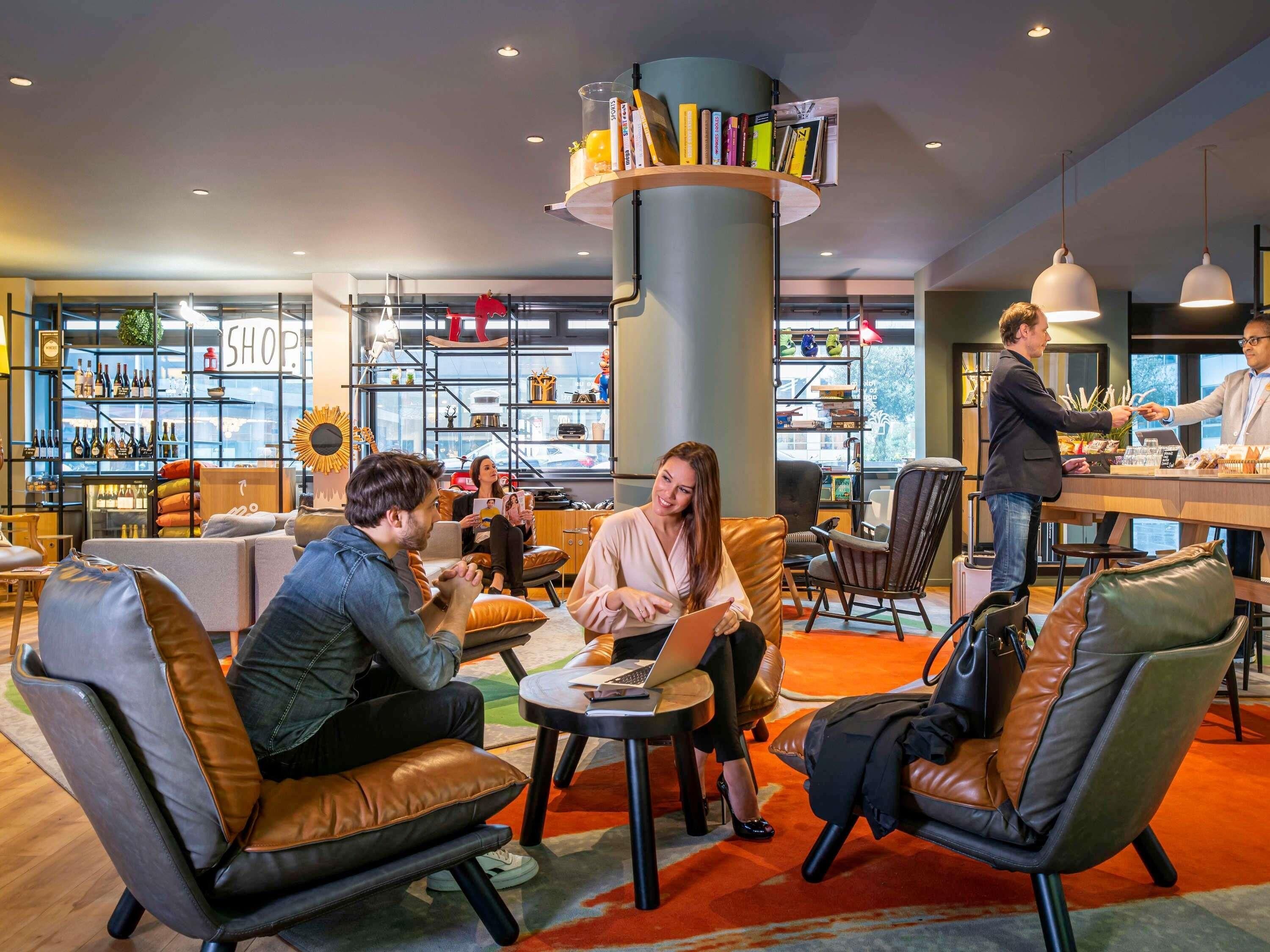 Un'area lounge moderna con sedute in pelle, una colonna centrale piena di libri e un angolo bar.