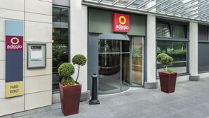 The exterior of the Adagio City Apartment Hotel with a modern design, featuring a glass entrance, signage, and potted plants.